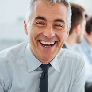 Confident professional businessman smiling at camera, office and business team working on background, selective focus