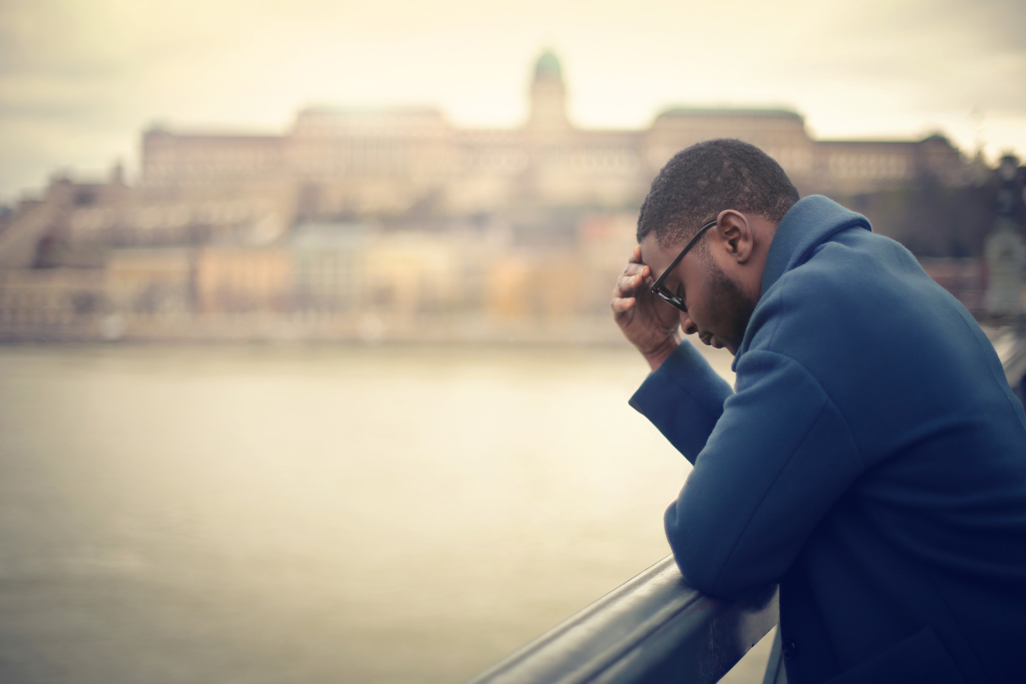 Man holding his head standing on a bridge
