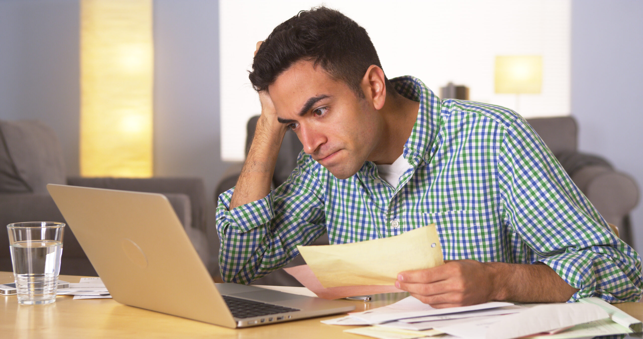 Frustrated man reviewing paperwork and working on a laptop