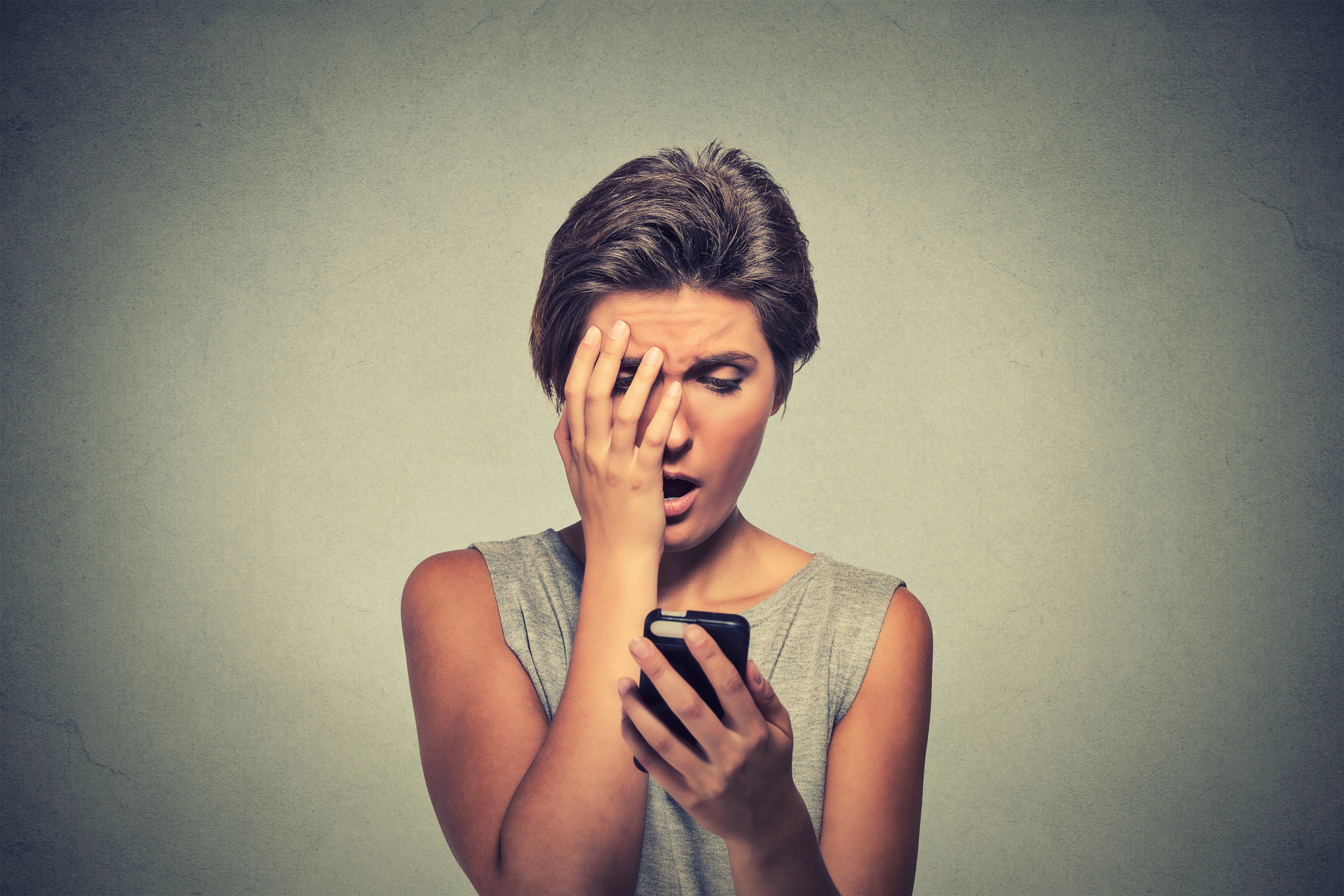Distressed woman holding cellphone disgusted shocked by the message received
